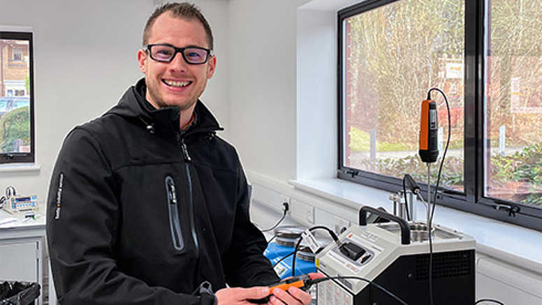 𝗪𝗲 𝗮𝗿𝗲 𝗾𝘂𝗮𝗹𝗶𝘁𝘆 𝗰𝗼𝗻𝘀𝗰𝗶𝗼𝘂𝘀! - Our values employee stands at desk and smiles