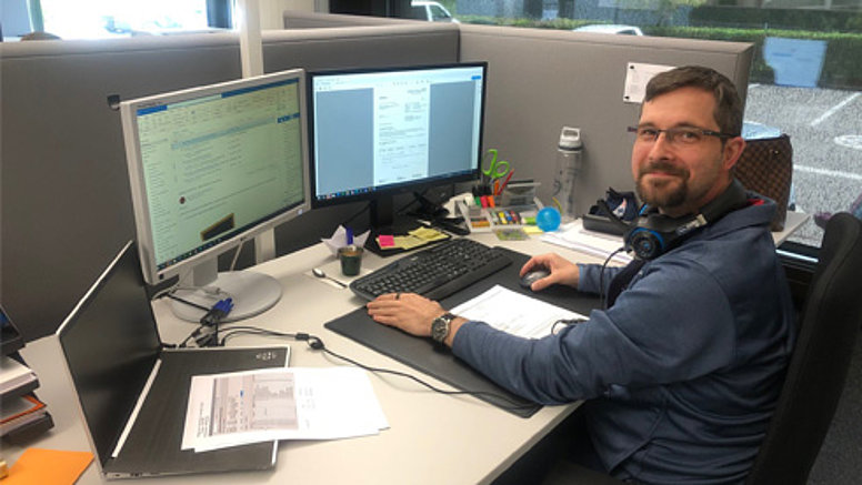We are international - Our values We are international - employee sits at desk and smiles.